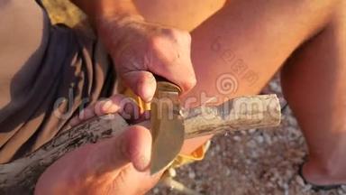 年轻的白种人希普斯特人用刀子雕刻木头，在海滩上制造<strong>一个</strong>木制<strong>勺子</strong>。 老年学校